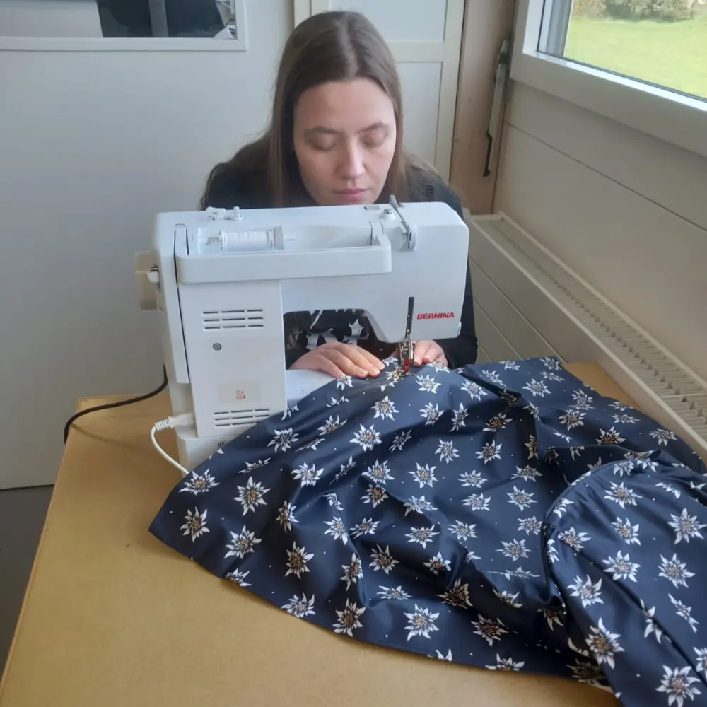 Junge Frau konzentriert sich auf das Nähen eines Edelweiss-Schürzenstoffs an einer BERNINA-Nähmaschine in einem hellen Schweizer Atelier.