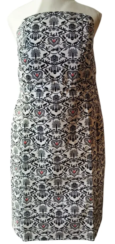 Handgefertigte Schweizer Schürze ohne Nackenband, traditionelles schwarz-weißes Muster inspiriert vom alpinen Scherenschnitt, mit roten Details in Herzform – präsentiert auf einer Schaufensterpuppe.